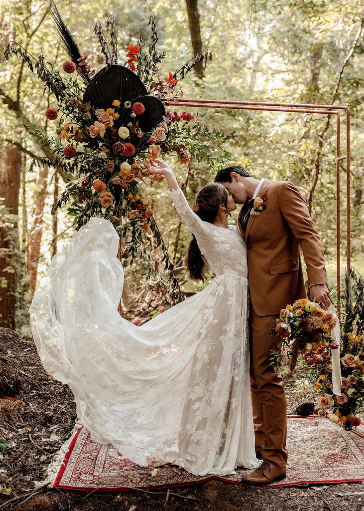 Bride wearing the Ari long sleeve low back bohemian style wedding dress kissing groom in the forest