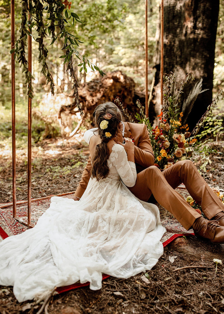 Groom kissing bride wearing the Ari long sleeve low back bohemian style wedding dress in forest