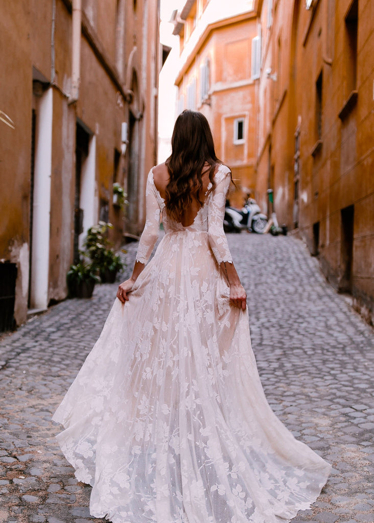 Bride on cobblestone street wearing the Ari long sleeve low back boho wedding dress