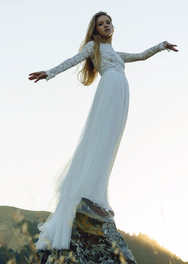 Bride wearing Zoey 2.0 dress standing on top of a rock, holding her arms out, looking at the camera