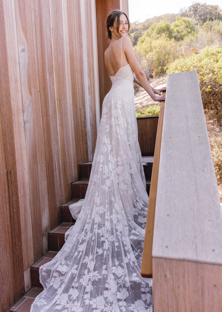Smiling bride wearing Lilith Dress on stairs, showing full length of train