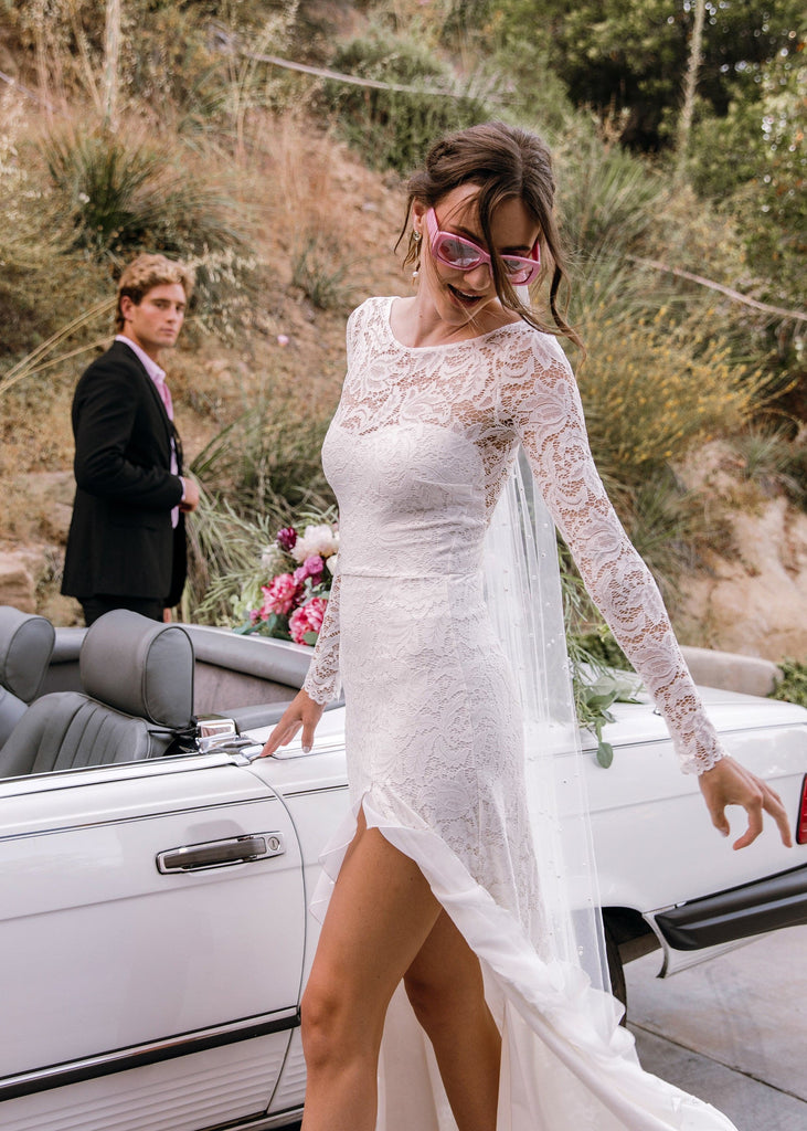 Bride in pink sunglasses wearing Sasha Dress in front of white convertible, groom in background 