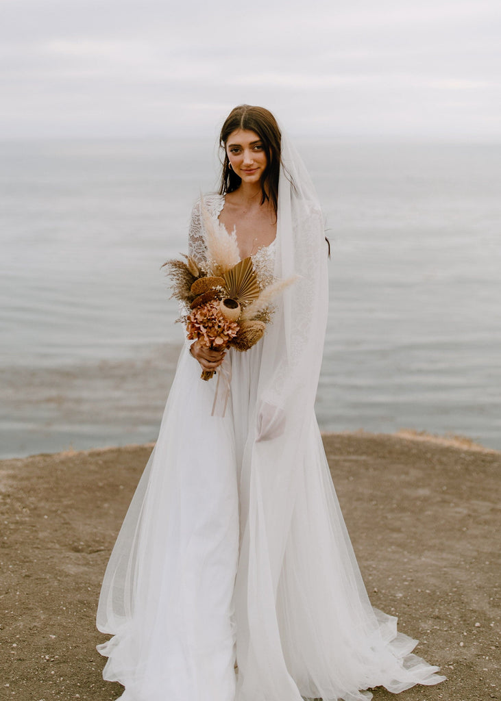 Bride standing on a cliff overlooking the ocean wearing Kenna chiffon veil and Indy dress