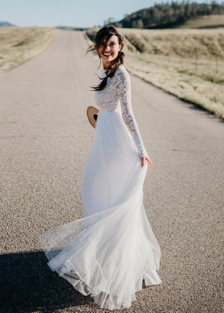 Bride holding hat and smiling on road wearing Zoey 2.0 dress