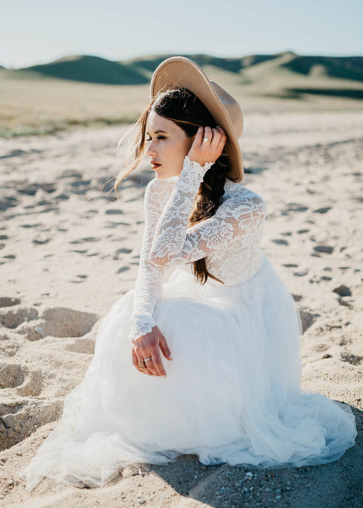 Bride in hat sitting on beach wearing Zoey 2.0 dress