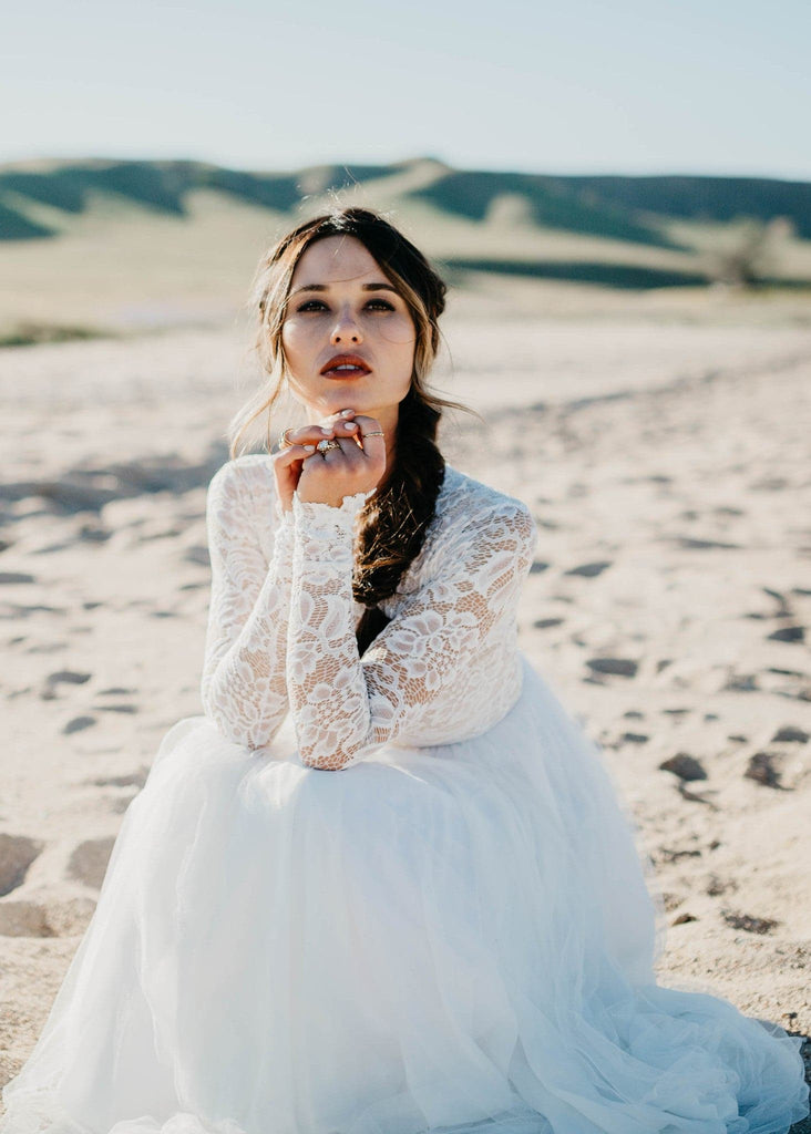 Bride sitting on beach wearing Zoey 2.0 long sleeve bohemian style wedding dress