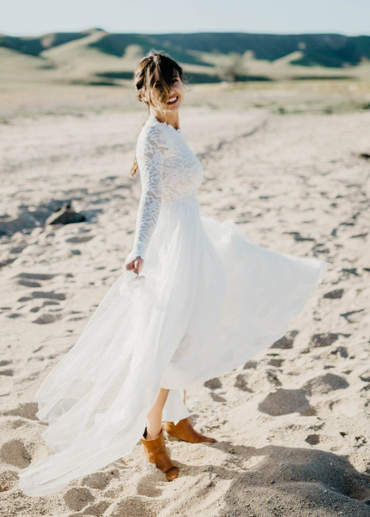 Bride in boots and Zoey 2.0 dress standing on beach and smiling