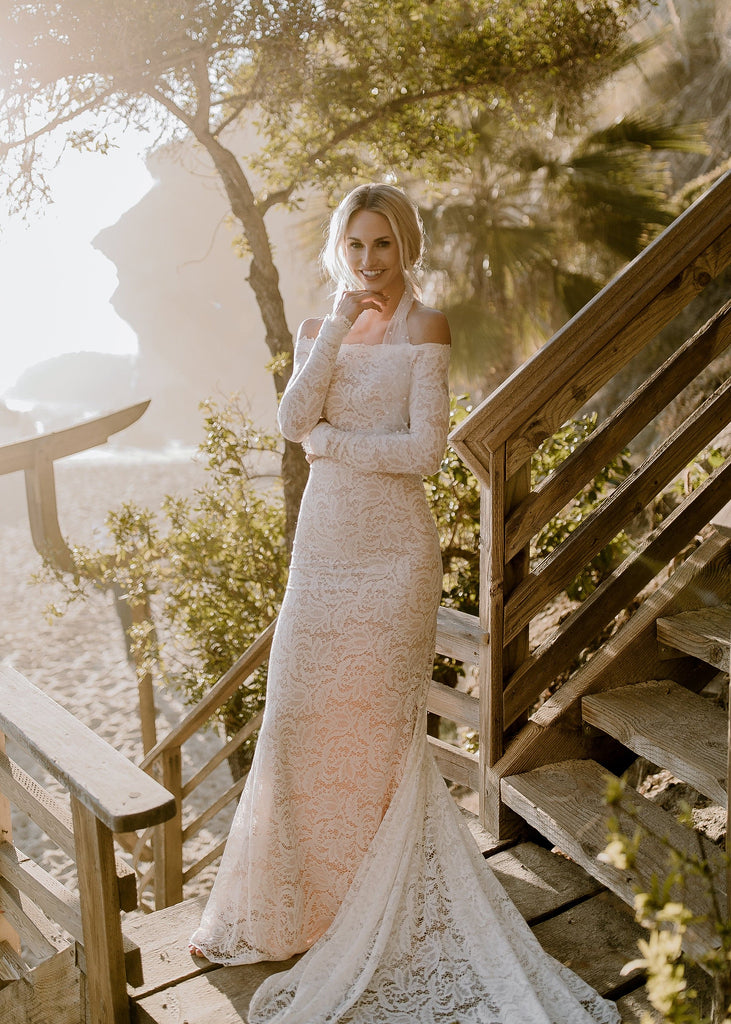 Blonde bride wearing Ayla dress standing on stairs leading to beach