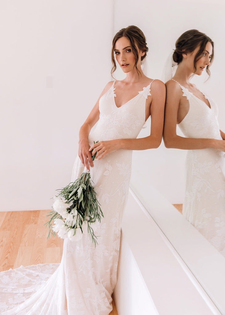 Bride wearing Lilith Dress holding bouquet leaning against mirror wall