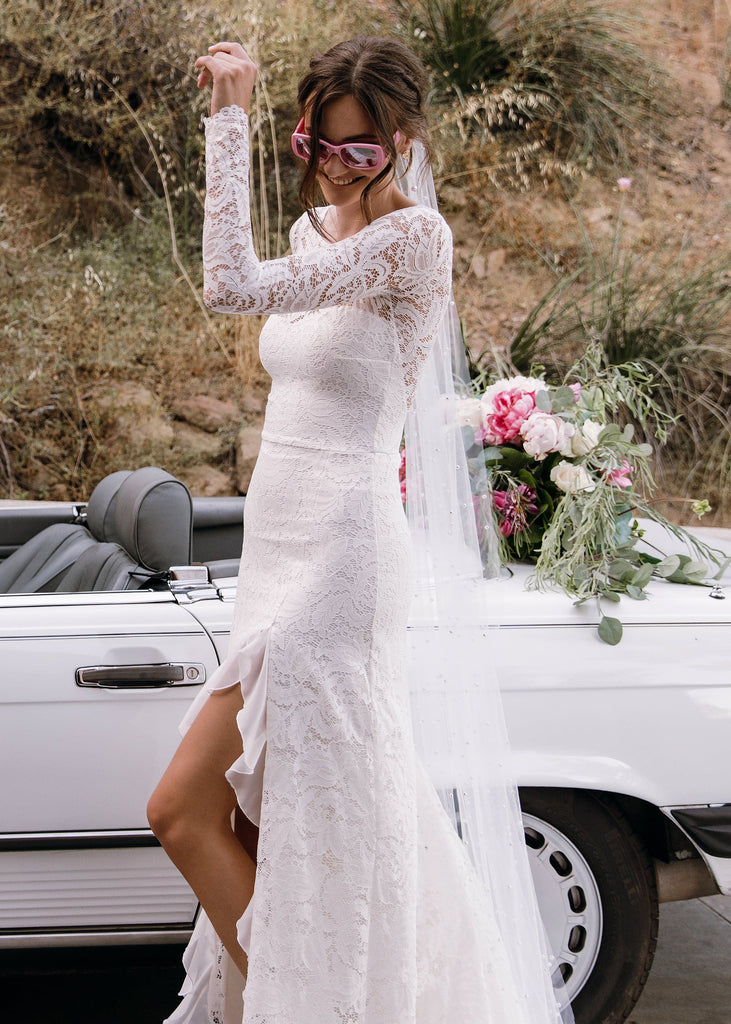 Bride in pink sunglasses wearing Sasha Dress, smiling and showing leg in front of white convertible