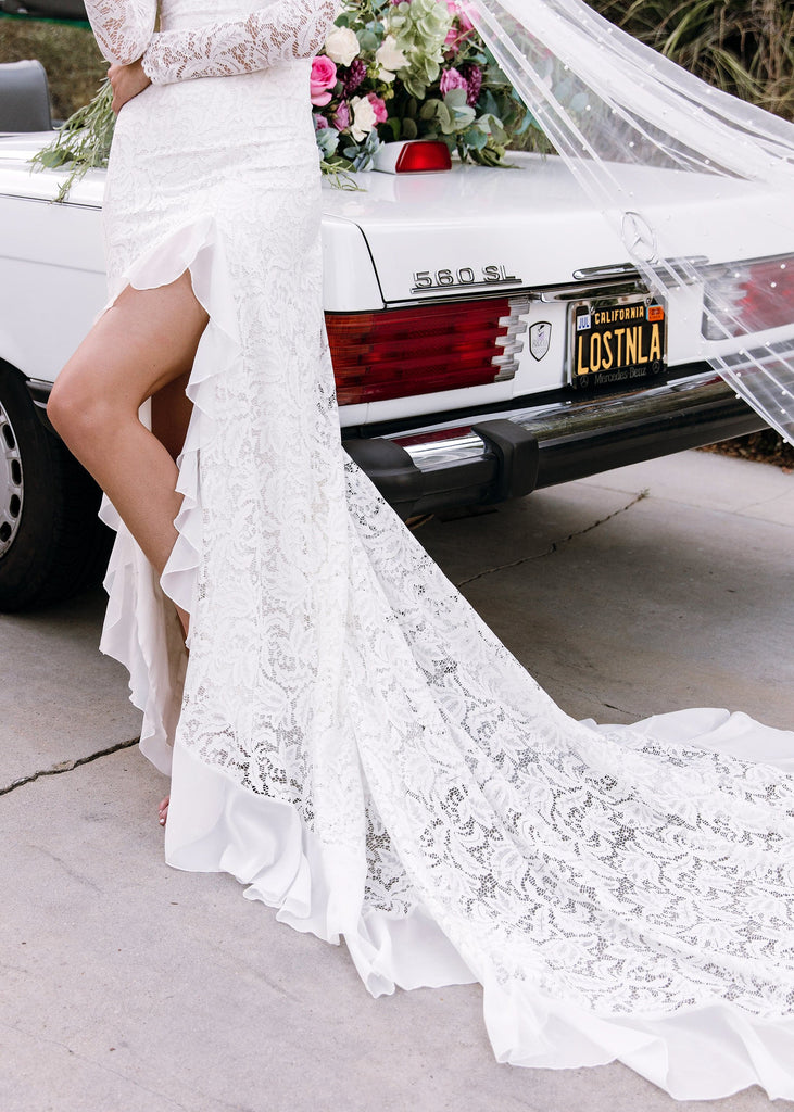 Lower body view of bride wearing Sasha Dress showing her leg leaning against white convertible