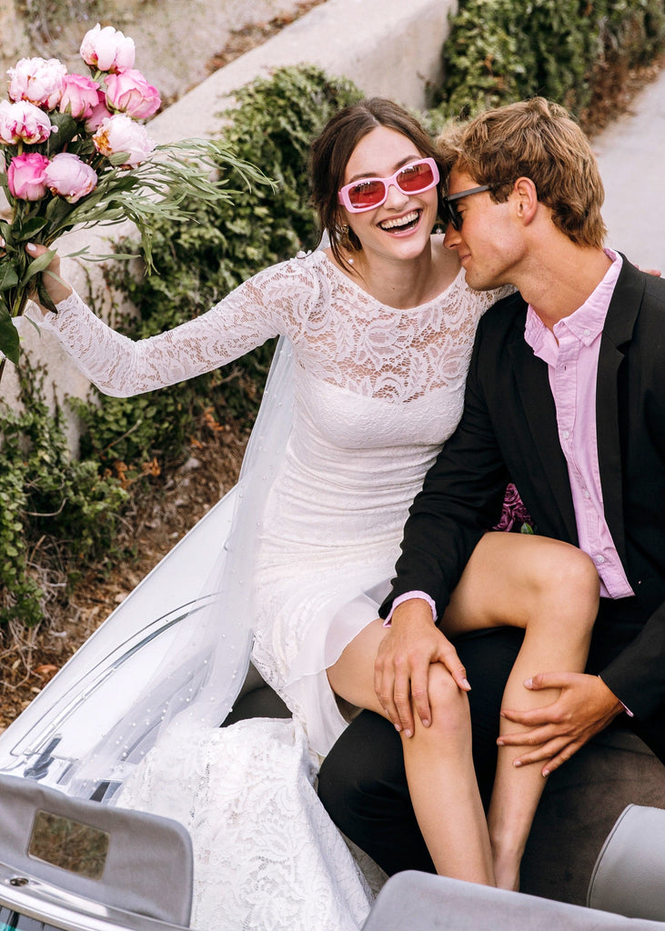 Bride in pink sunglasses wearing Sasha Dress laughing in the back of white convertible with groom